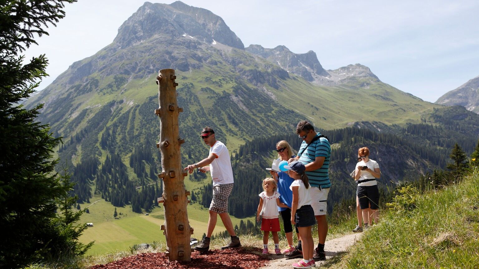 Eine Familie steht vor einer Station am Grünen Rätsel-Ring mit Omeshorn im Hintergrund