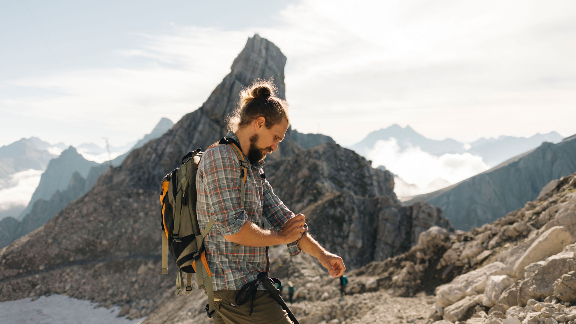 Wanderer steht am felsigen Grat und im Hintergrund ist ein weitläufiges Gebirgspanorama zu sehen