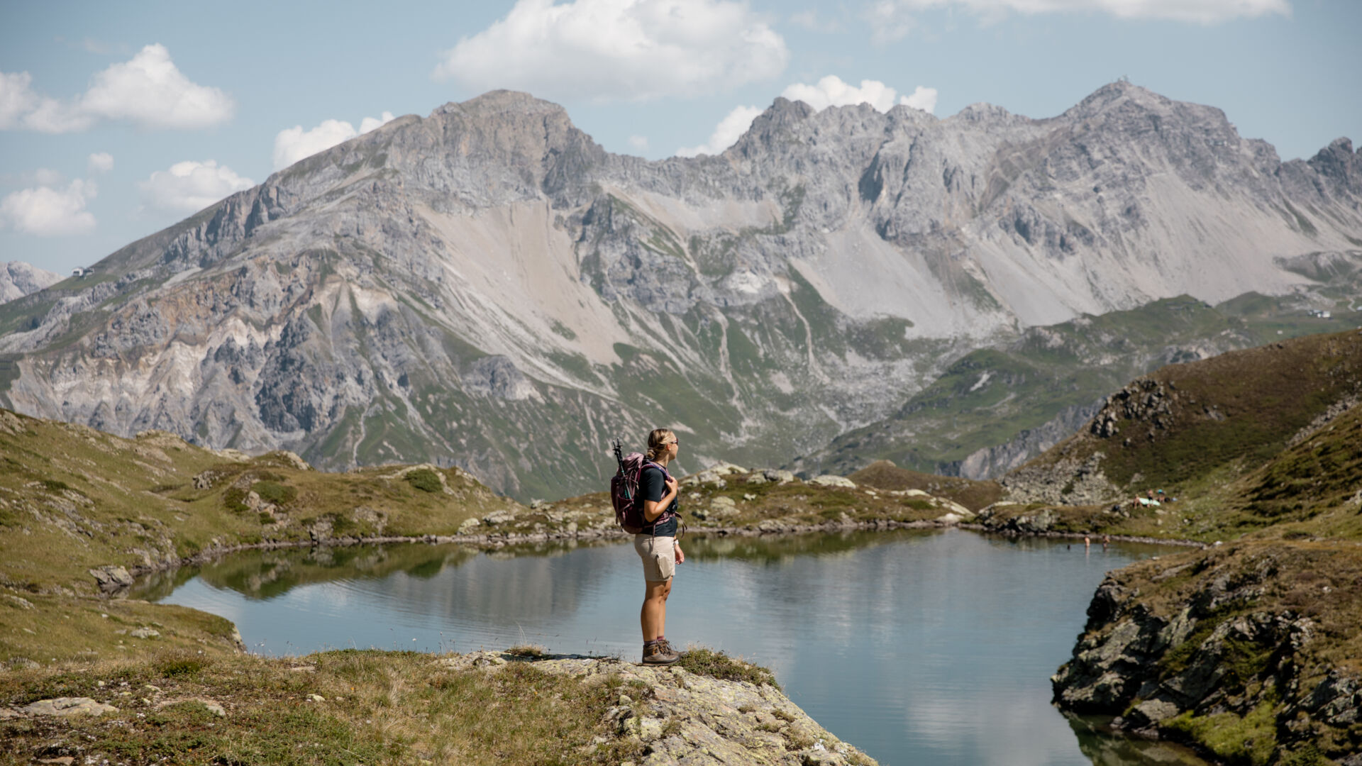 Wanderin mit Rucksack steht am Ufer des Unteren Maroisees und blickt auf die schroffe Bergkette dahinter.