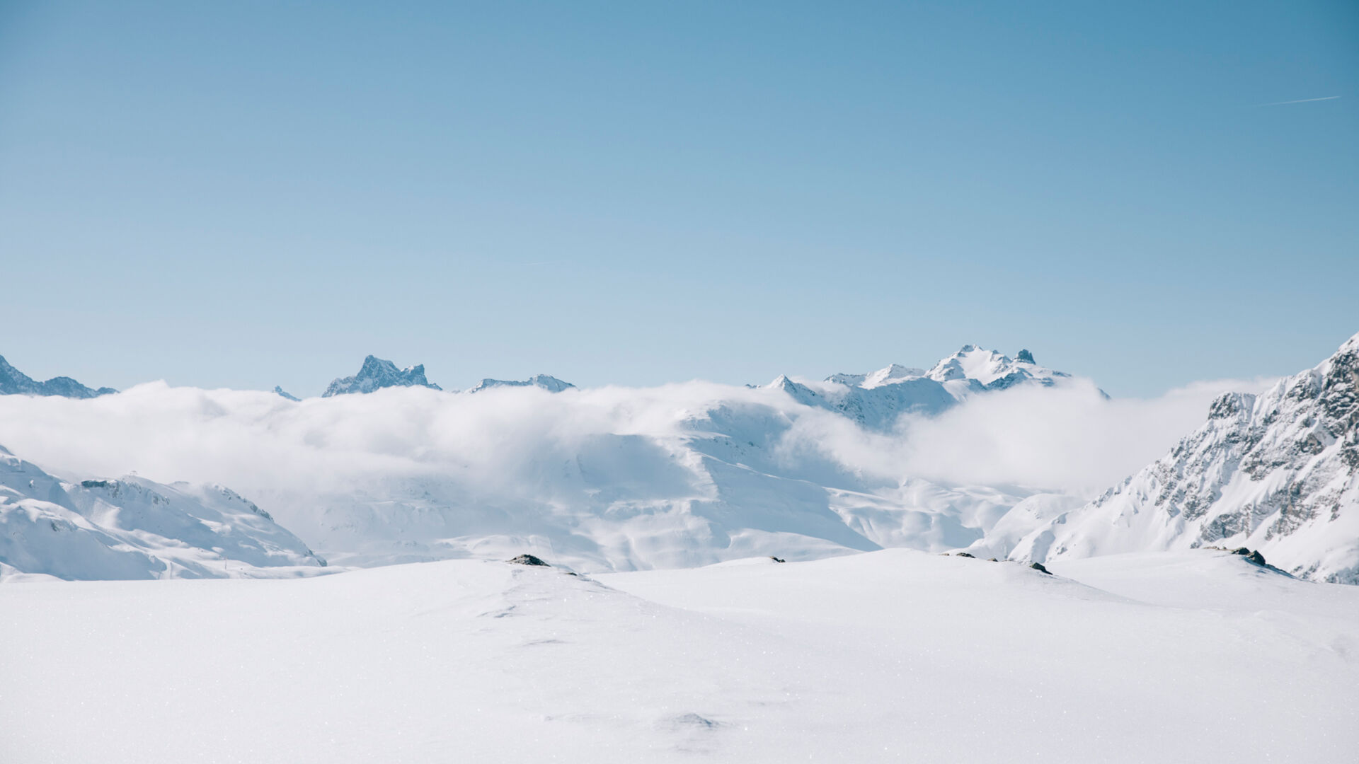 die verschneiten Berggipfel ragen aus der Wolkendecke in den klar blauen Himmel