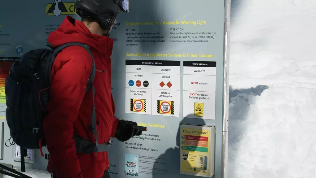 Ein Mann in Skiausrüstung steht vor demFreeride Safety Check Punkt im Skigebiet Ski Arlberg