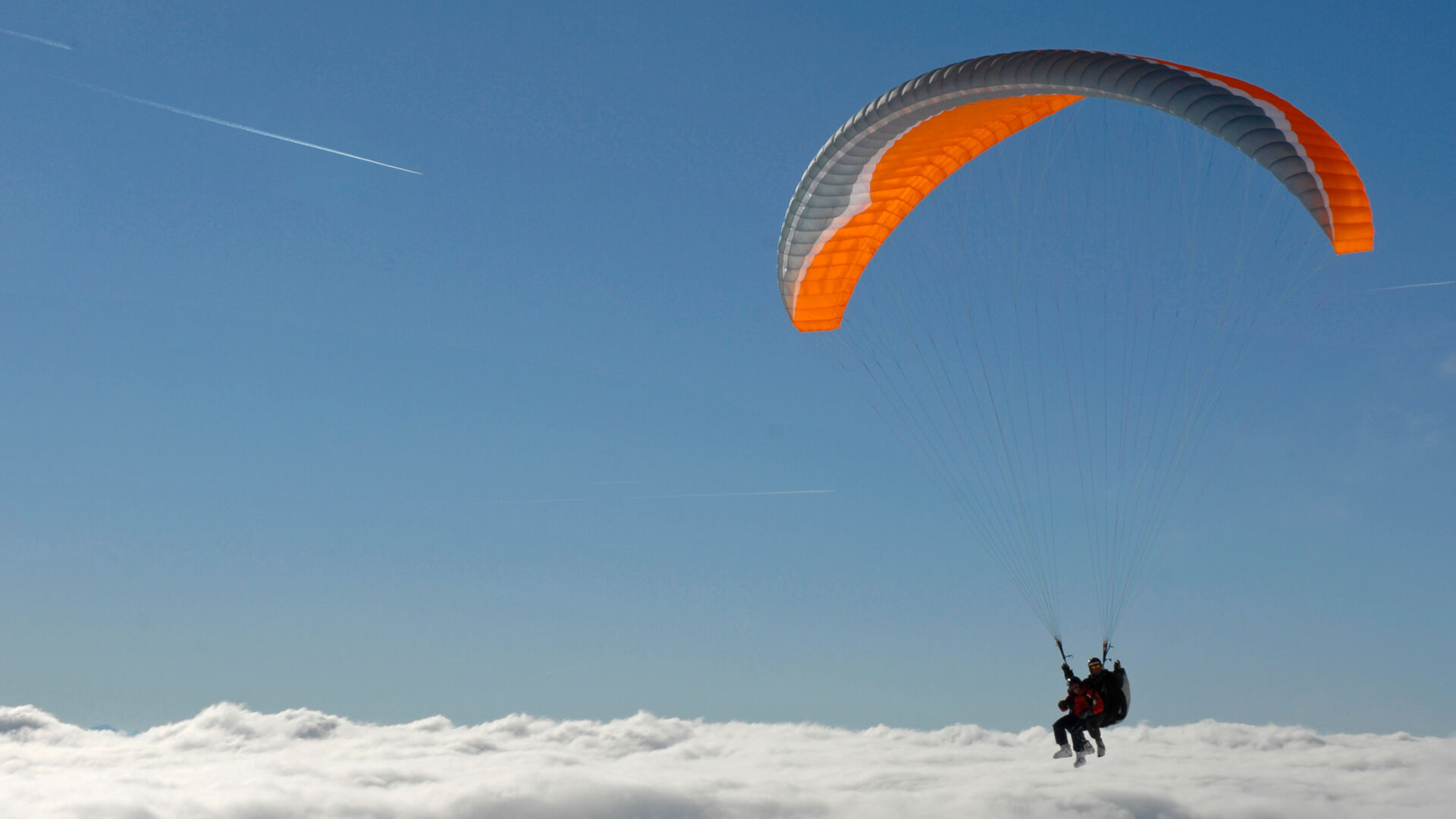 Zwei Tandemflieger im Gleitschirm über der Wolkendecke und strahlend blauen Himmel