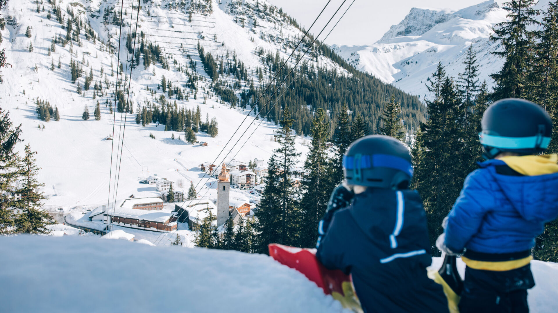 Kinder rodeln mit dem Zipfelbob in Lech Zürs auf der Rodelbahn mit Blick auf das Dorf