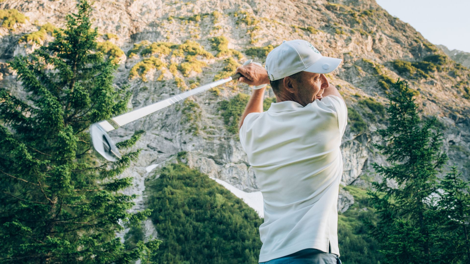 Golfer schwingt den Golfschläger am Zuger Golfplatz mit felsigem Berg im Hintergrund