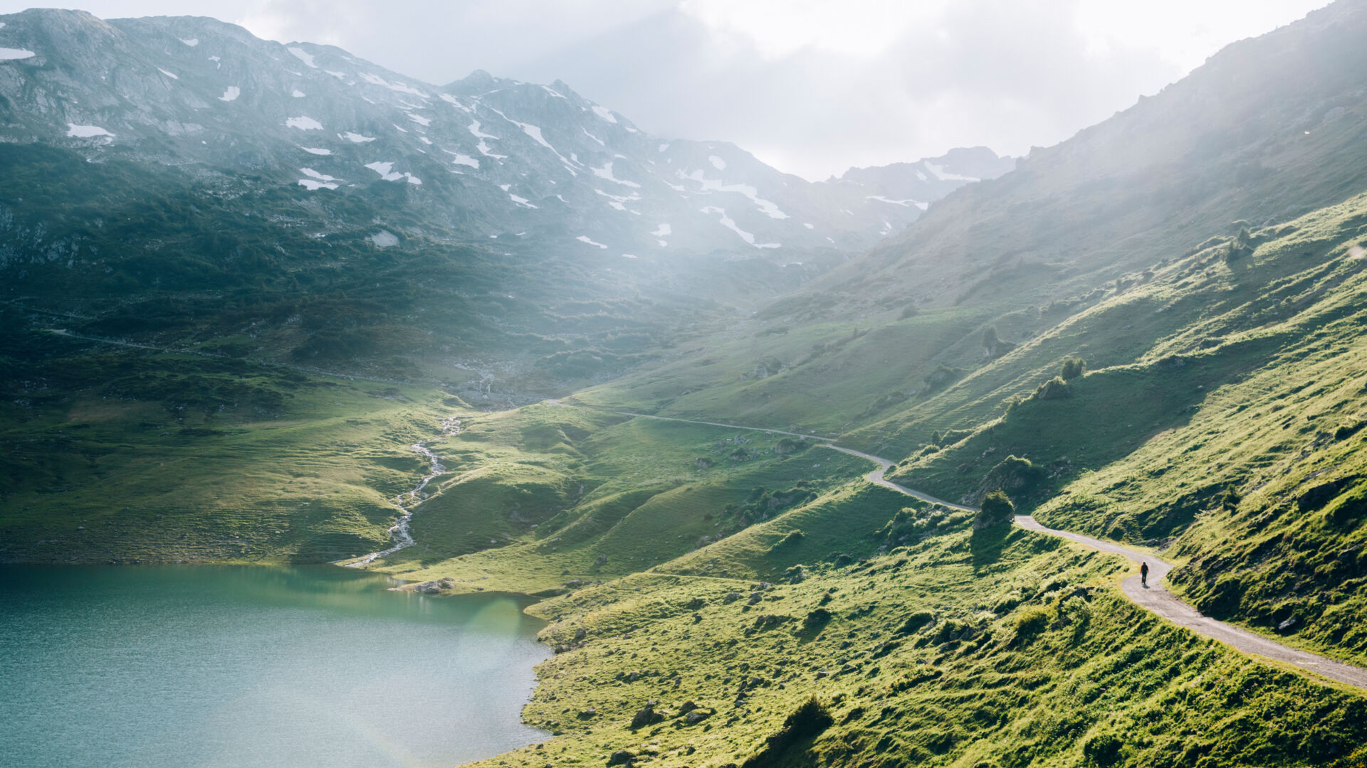 ein Wanderweg führt durch die grünen Bergwiesen über dem Formarinsee vorbei