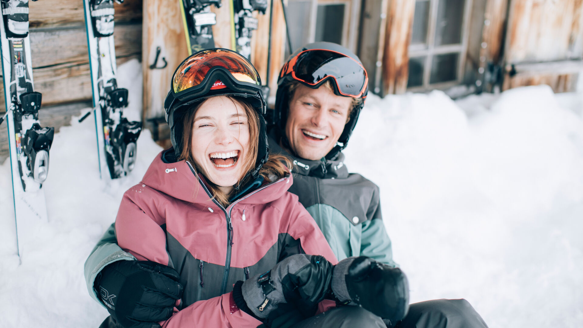 ein junges Paar liegt gemeinsam im Schnee und lacht