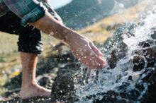 Abkühlung im frischen Bergwasser Eine Hand berührt klares Bergwasser