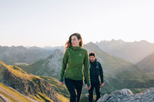 Ein Paar wandert bei Morgensonne mit einem weitl&auml;ufigen Gebirgspanorama im Hintergrund