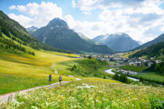 Zwei Wanderer gehen am Lechweg entlang, mit dem Dorf Lech im Hintergrund