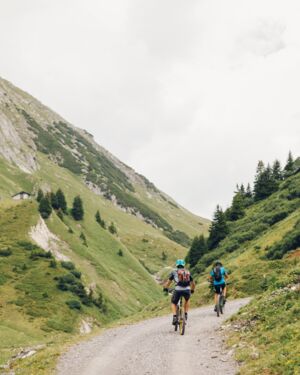 Zwei Radfahrer fahren auf einem Schotterweg durch ein Tal in den Bergen.