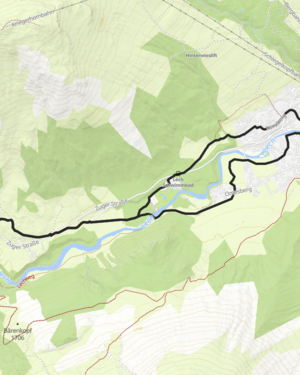 Blick auf den Winterwanderweg, der neben den verschneiten Nadelbäumen und den winterlichen Bergkulissen entlang geht