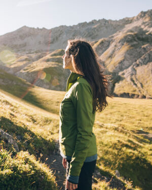 Frau schaut der Sonne entgegen und im Hintergrund erstreckt sich eine wunderschöne Berglandschaft