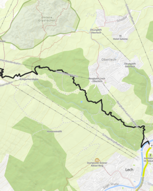 Zwei Radfahrer fahren einen Schotterweg im Gebirge hinab. Im Hintergrund erstrecken sich die weitläufigen Berge.