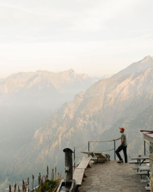 Ein Wanderer steht auf der Terrasse einer H&uuml;tte und blickt auf das Bergpanorama.