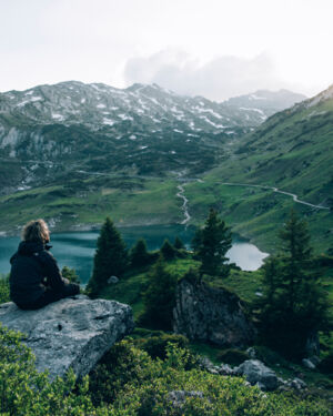 ein Wanderer genießt die Aussicht auf den Formarinsee während die ersten Sonnenstrahlen zwischen den Bergen scheinen