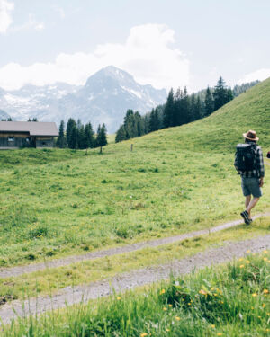 zwei Personen wandern &uuml;ber den Wanderweg in Oberlech in Richtung einer Holzh&uuml;tte mit Blick auf das Omeshorn