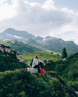 ein Wanderer macht eine Pause und genie&szlig;t das traumhafte Bergpanorama inmitten von saftig gr&uuml;nen Wiesen