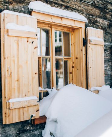 Blick auf ein eingeschneites Fenster einer urigen Holzhütte