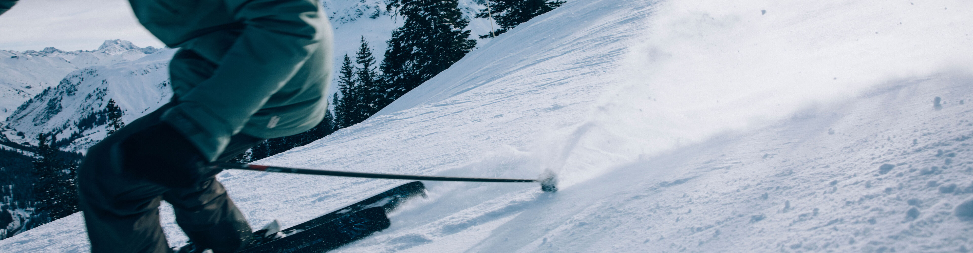 Nahaufnahme, wie ein Skifahrer über der präparierten Piste eine kleine Staubwolke nachzieht