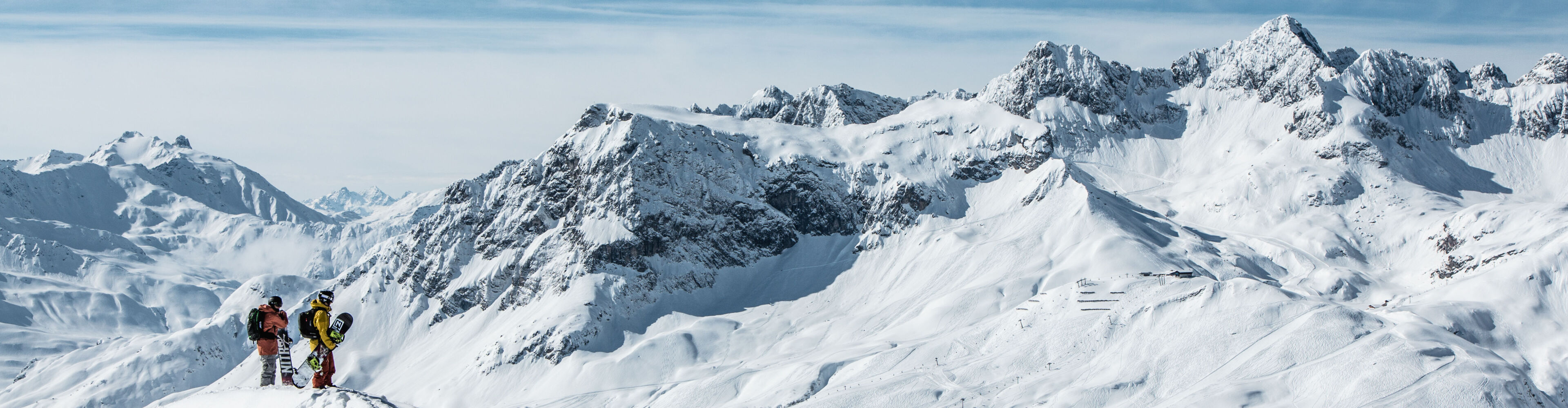 zwei Snowboarder stehen am Tiefschneehang und genießen die traumhafte Aussicht auf die verschneite Bergkulisse von Lech Zürs am Arlberg