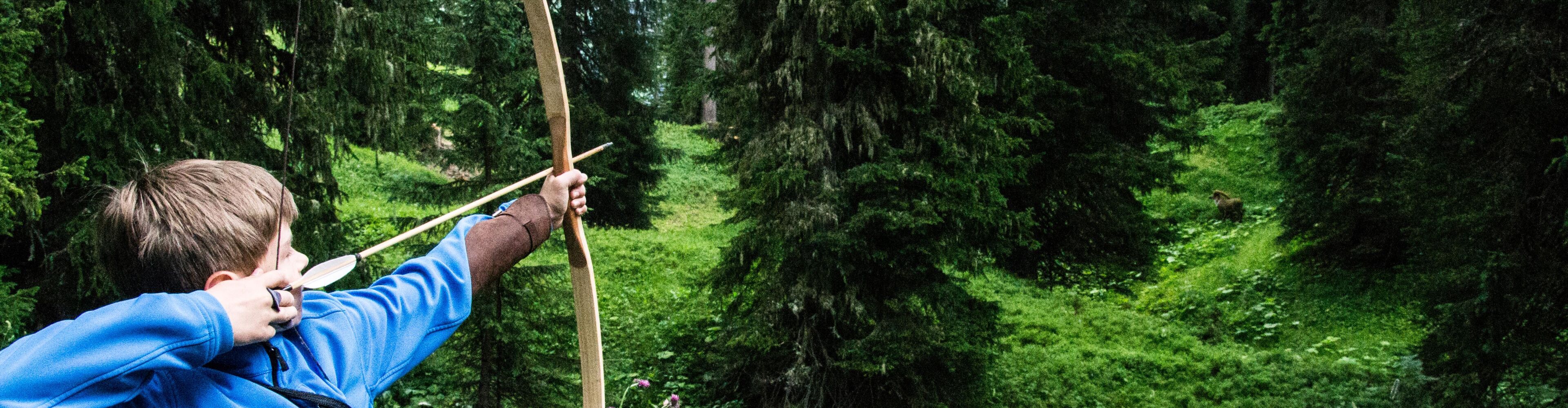Kind spannt den Bogen im Wald beim Bogenschießen