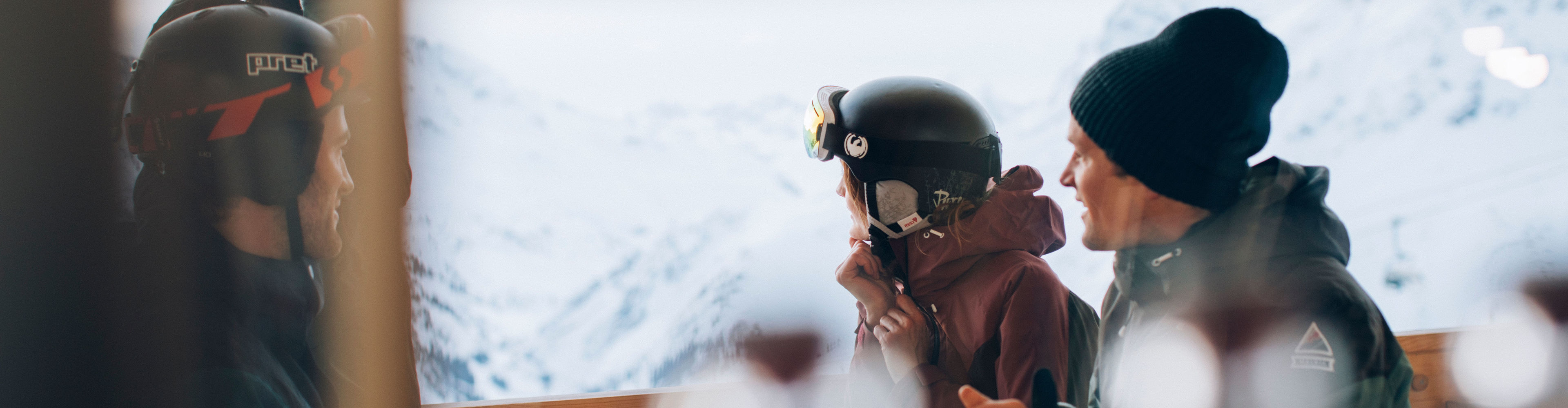vier Freunde sitzen auf der Sonnenterrasse der Skihütte und genießen das verschneite Bergpanorama