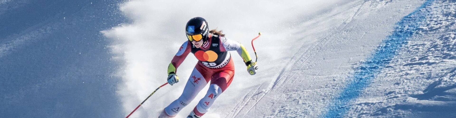 Skifahrerin fährt über steile Piste in Rennanzug bei Skirennen und dreht in die nächste Kurve ein