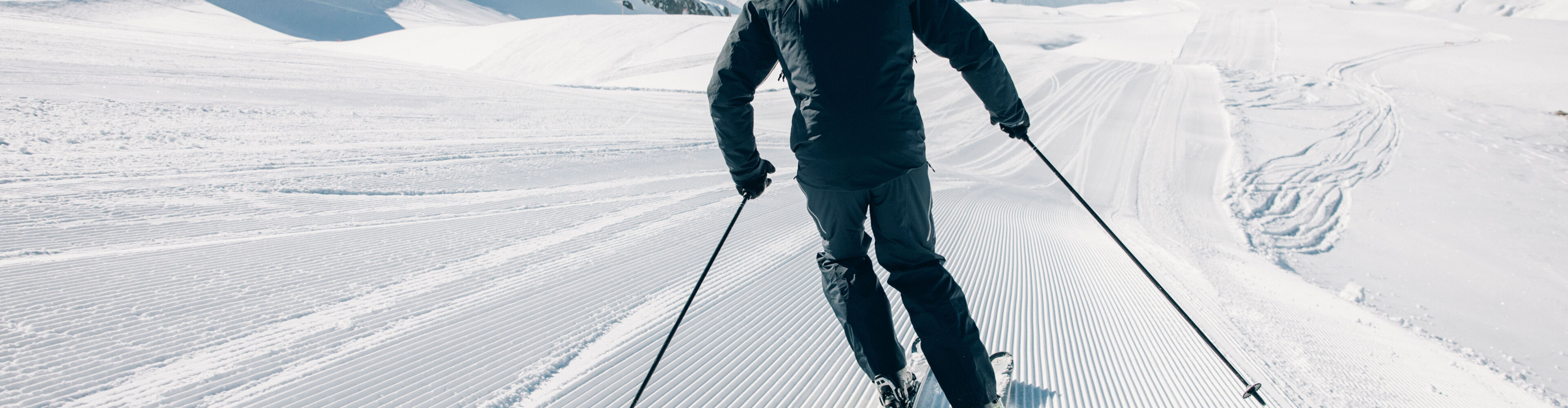 ein Skifahrer fährt über die frisch präparierte Skipiste mit einer traumhaften Aussicht auf das winterliche Bergpanorama