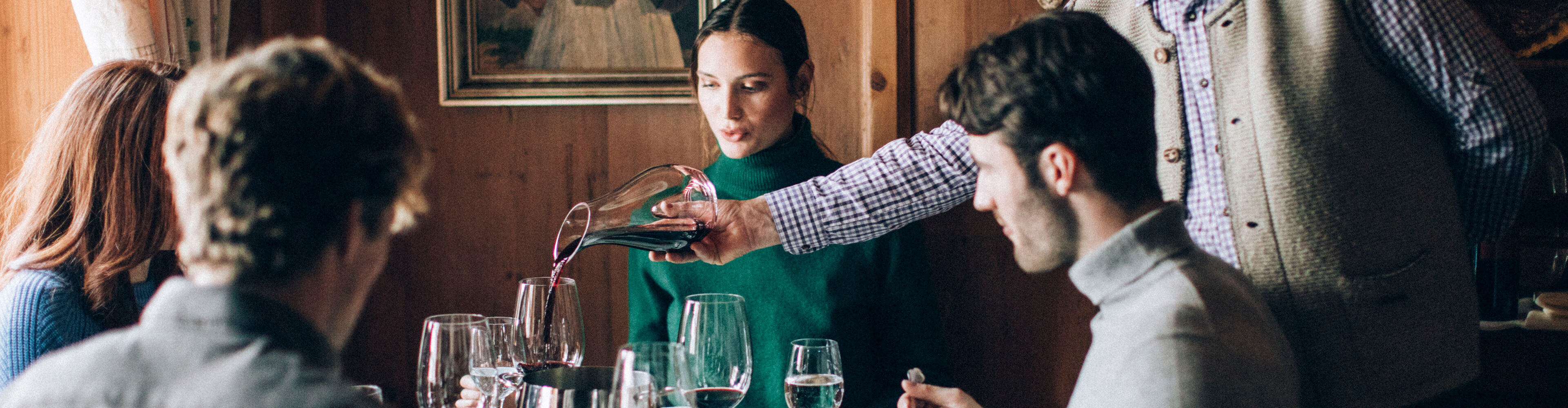vier Freunde genießen ihren Fondueabend in einer gemütlichen Gaststube, während der Gastwirt ihnen ein Glas Rotwein einschenkt