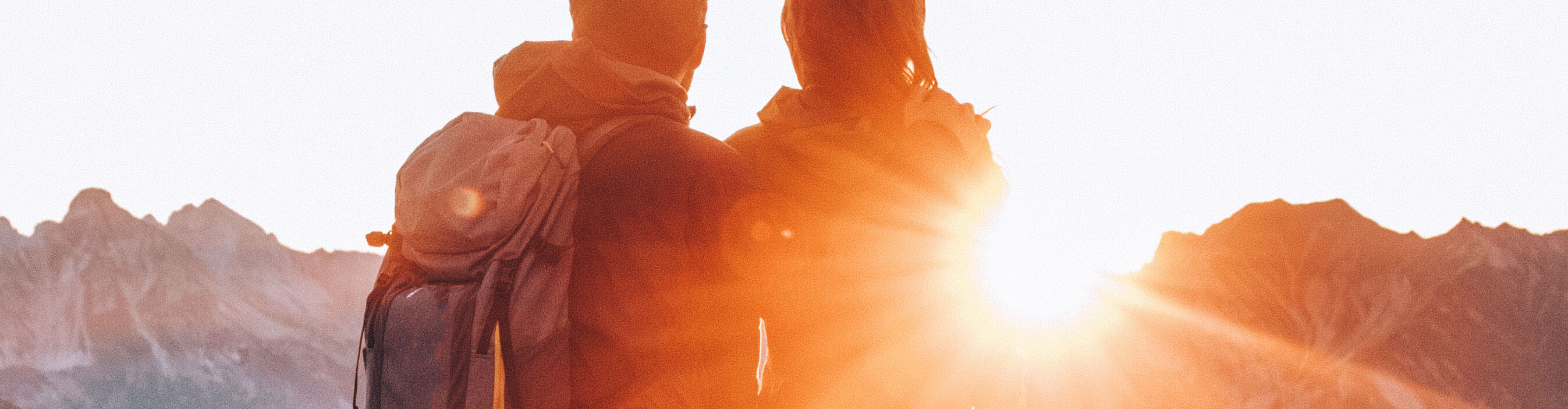 Ein Paar steht am Gipfel eines Berges, blickt in die Ferne und beobachtet den Sonnenaufgang am Horizont.