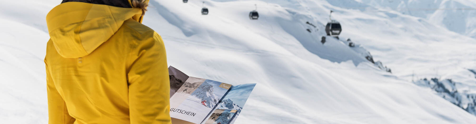 eine Skifahrerin steht im Skigebiet und hält eine Karte in der Hand