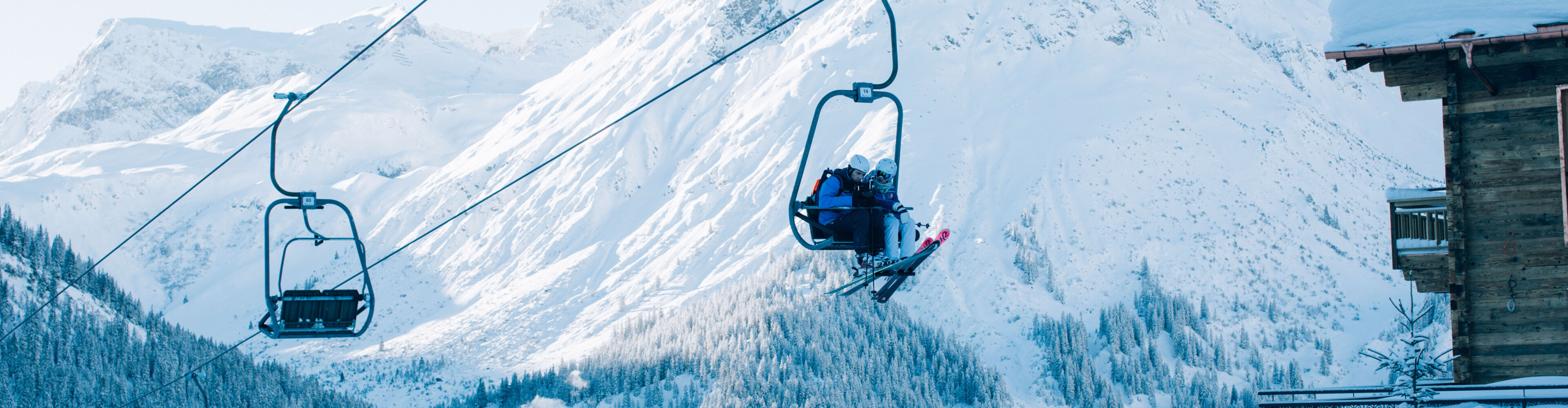 zwei Skifahrer fahren mit dem Sessellift in das Skigebiet, während man im Hintergrund das traumhafte Omeshorn und Lech sieht