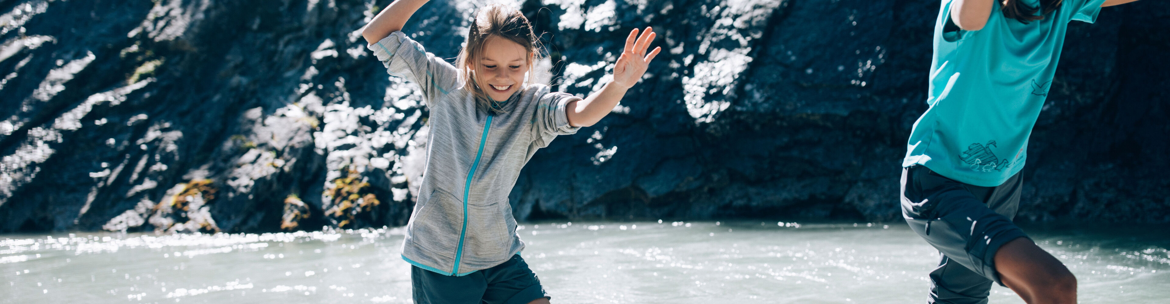 Zwei Kinder toben barfuss im Lech im Sommer