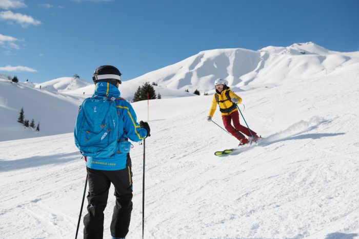 zwei Skifahrer fahren über die Piste in Lech und im Hintergrund sieht man die traumhafte Winterlandschaft