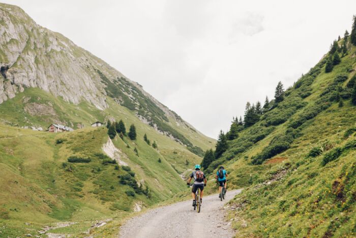 Zwei Radfahrer fahren auf einem Schotterweg durch ein Tal in den Bergen.