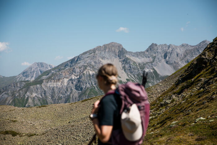 Trailrunnerin mit Rucksack auf einem alpinen Wanderweg vor der beeindruckenden Bergkulisse des Arlbergs.