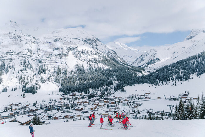 mehrere Personen des Skiclubs genießen die traumhafte Aussicht auf Lech und die verschneite Bergkulisse im Hintergrund