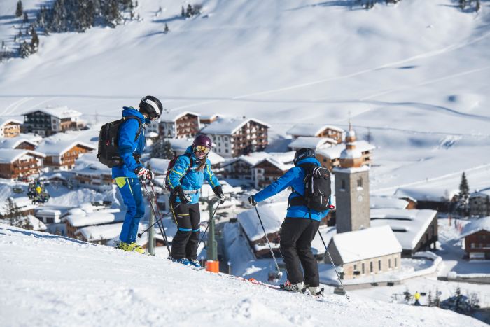 drei Skifahrer stehen auf der Piste mit Blick auf das Dorf Lech