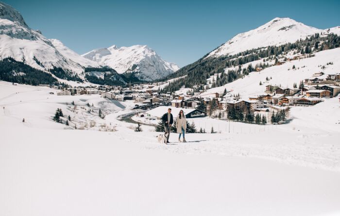 zwei Personen machen einen Winterspaziergang am Flühenweg mit Blick auf das Dorf
