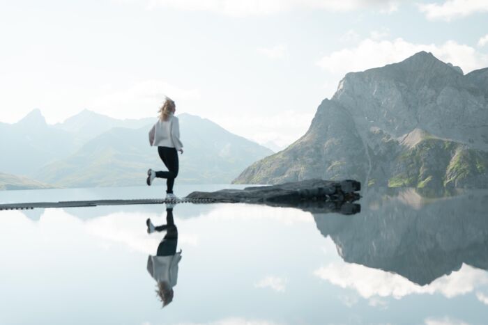 Frau auf Felsen in einem spiegelnden Bergsee vor schroffem Alpenpanorama.