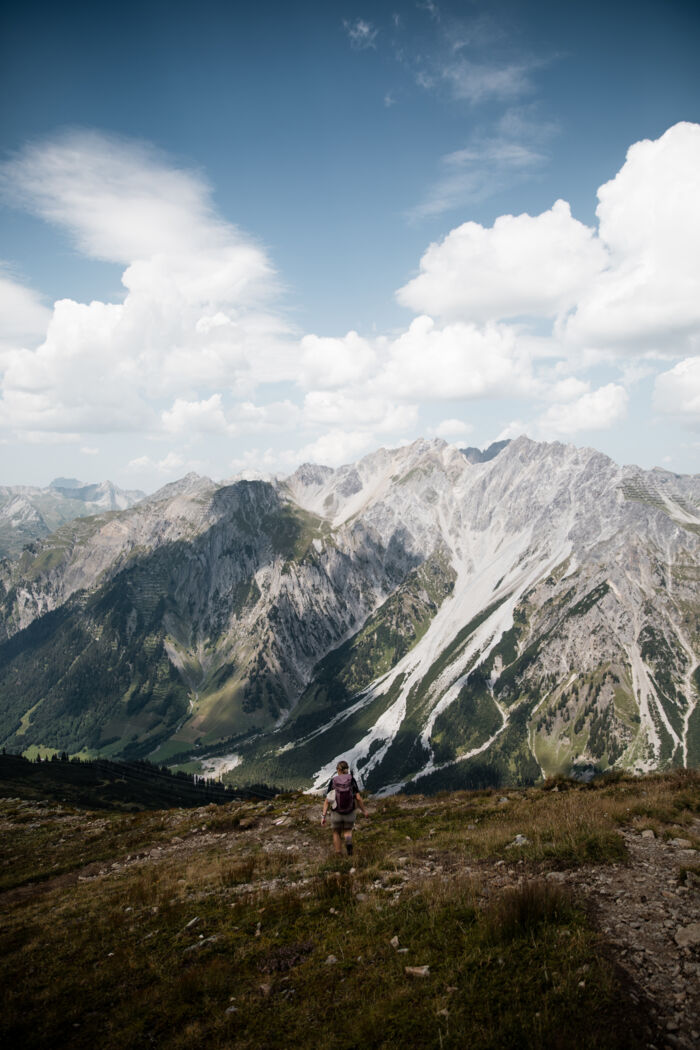 Wanderin mit Rucksack auf einem alpinen Bergpfad mit beeindruckender Bergkulisse und weitläufigem Blick über den Arlberg
