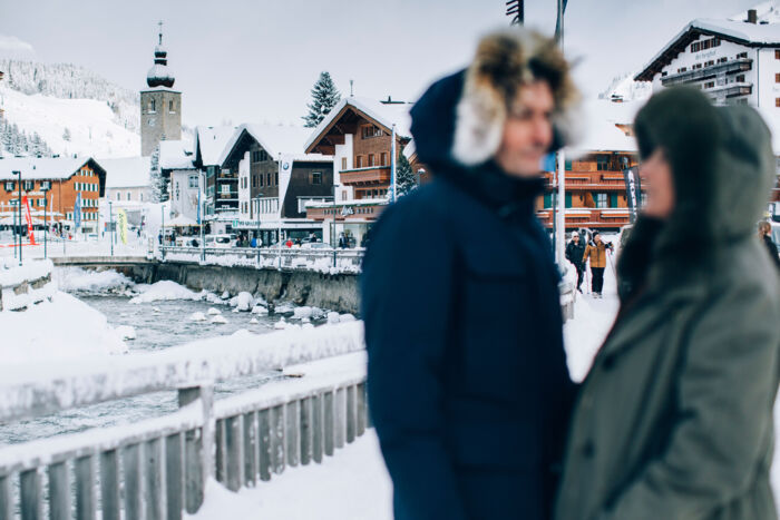 zwei Personen genießen einen ruhigen Moment zu Zweit beim Winterspaziergang durch das Dorf, während man im Hintergrund die schöne schneebedeckte Lechpromenade sieht