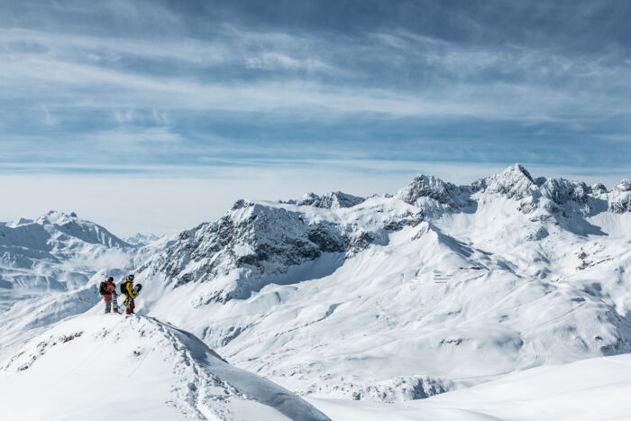 zwei Snowboarder stehen am Tiefschneehang und genießen die traumhafte Aussicht auf die verschneite Bergkulisse von Lech Zürs am Arlberg