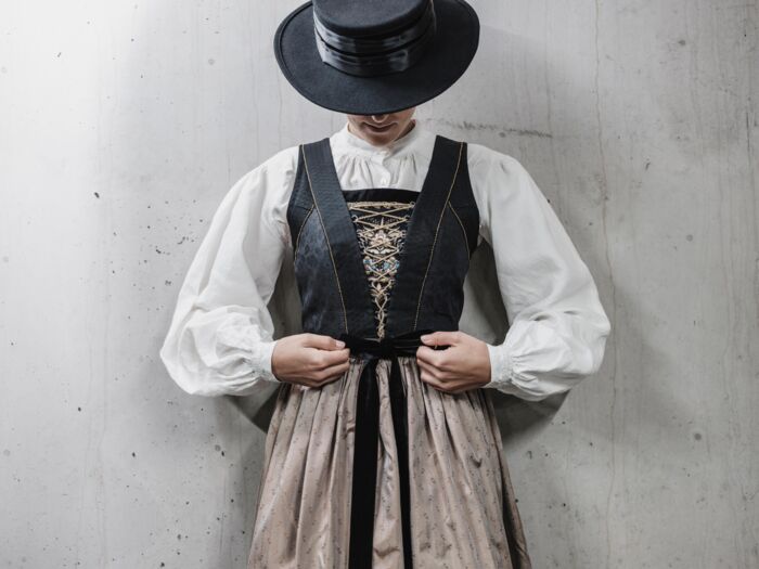 Frau in Walser Tracht mit schwarzen Wollrock, verziertem Mieder, Schürze und schwarzen Hut