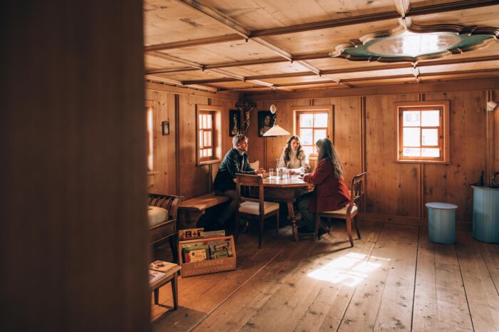 drei Personen sitzen an einem runden Tisch im Huber-Hus, in einem gemütlichen, urigen Ambiente