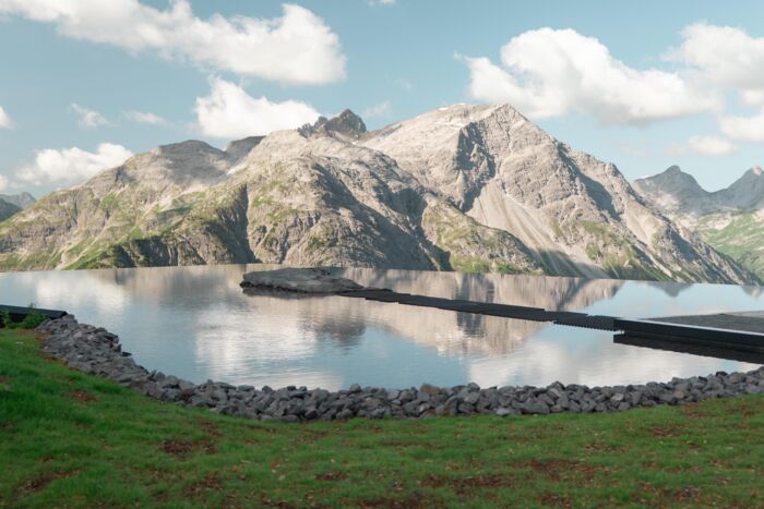 Frau auf Felsen in einem spiegelnden Bergsee vor schroffem Alpenpanorama.