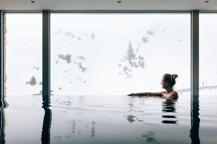 eine Frau genießt die winterliche Aussicht im Infinity Pool des Zürserhof mit Panoramablick auf Zürs