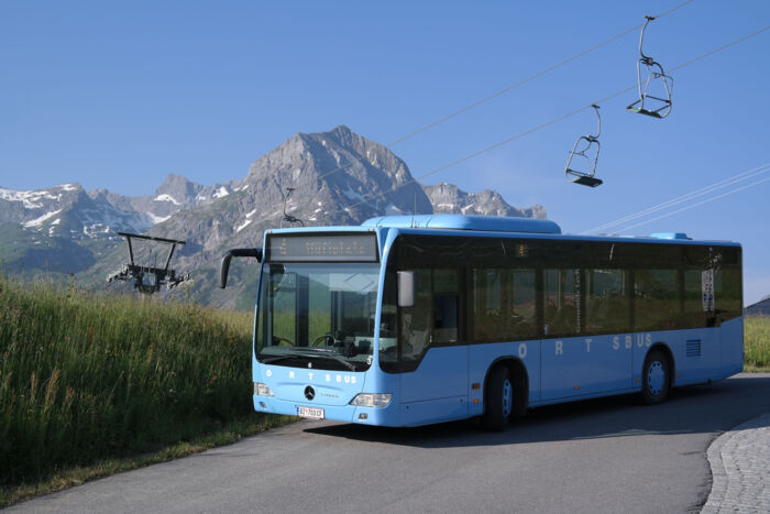 Im Vordergrund ist der blaue Ortsbus zu sehen und im Hintergrund das Omeshorn mit dem 2er Sessellift der Schlosskopfbahn