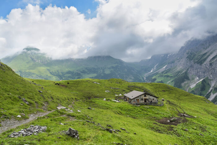 Ausblick auf eine Alpe, eingebettet in der Berglandschaft mit grünen Wiesen und Quellwolken am Himmel