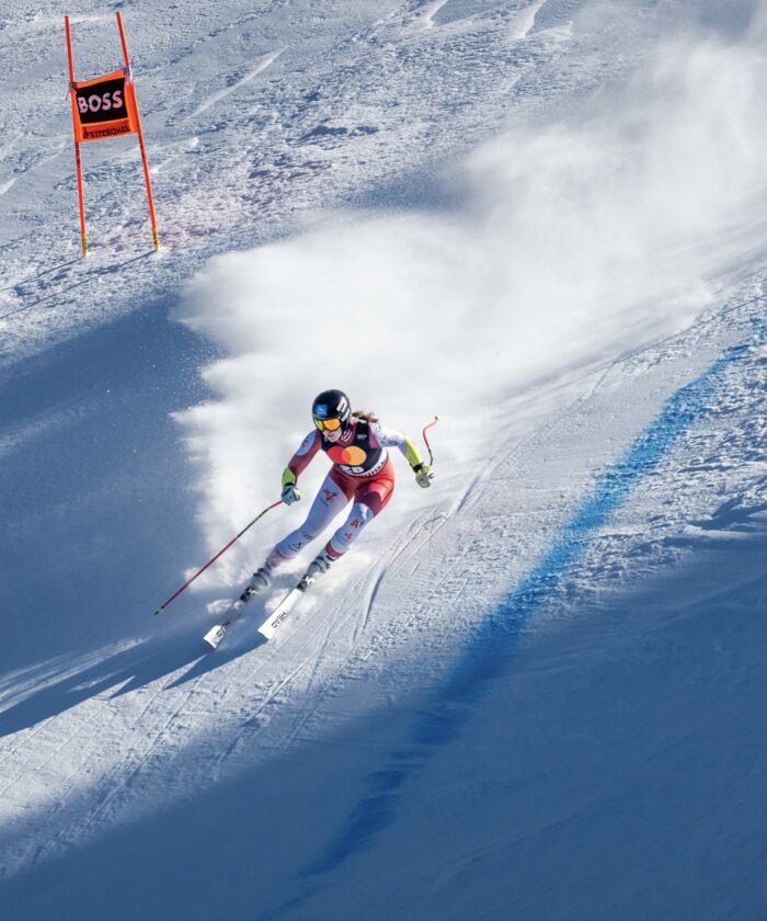 Skifahrerin fährt über steile Piste in Rennanzug bei Skirennen und dreht in die nächste Kurve ein